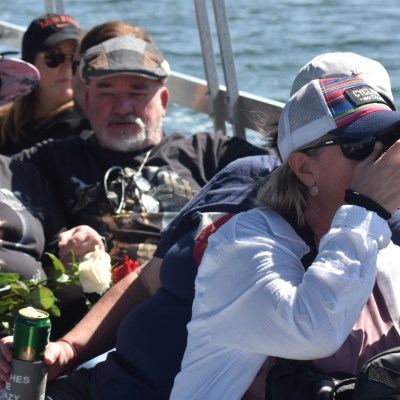 People seated on a boat, one photographing, holding a rose and beverage can.