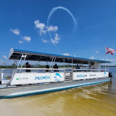 Tour boat on shore with people onboard; a skywriting loop visible against blue sky.