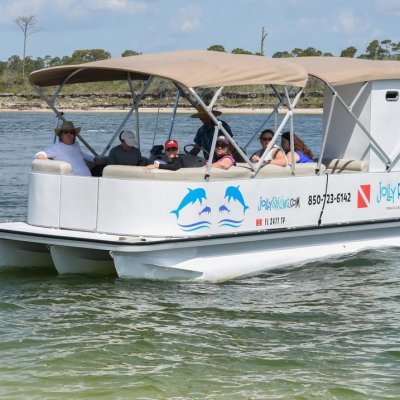 A pontoon boat with people on a calm lake near a wooded shoreline.