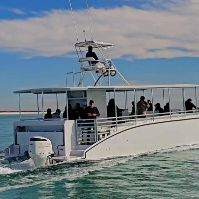 Catamaran with passengers on water, moving away from the shore under a clear blue sky.