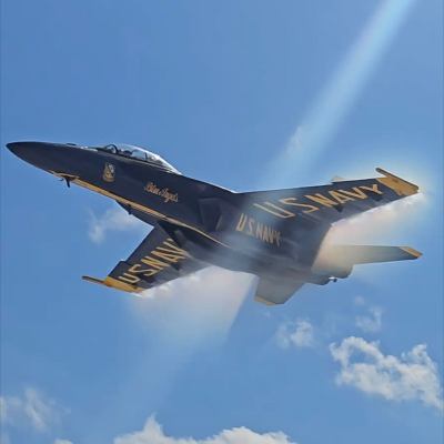 Jet labeled U.S. Navy performs a flyby with vapor cone effect under sunny sky.