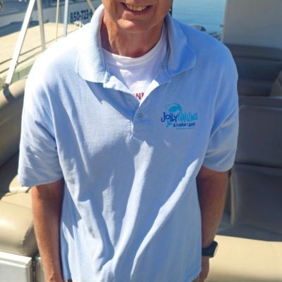 Person on a boat wearing sunglasses, a blue visor, and a light blue polo shirt with 'Jolly Sailing' logo.
