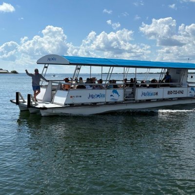 Tour boat with blue canopy on water, people aboard. Cloudy sky in background.