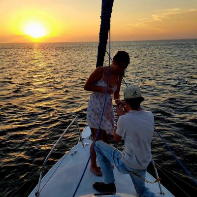 Person kneeling and proposing on boat at sunset, over calm ocean.