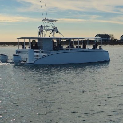 A catamaran boat on calm water near a coastline under a cloudy sky.