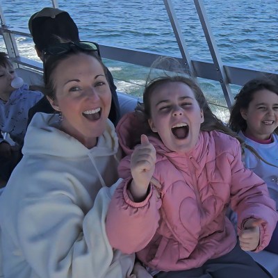 People smiling and cheering on a boat with water and shoreline in the background.