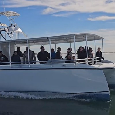 A white catamaran with passengers cruises on calm waters under a partly cloudy sky.