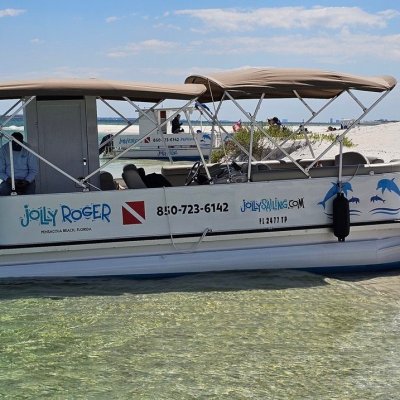Small boat named Jolly Roger docked near sandy beach with people sitting.