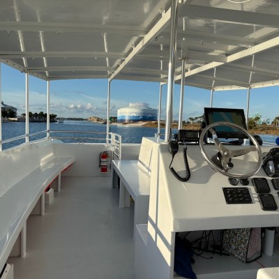 Boat interior with steering wheel and seats, overlooking water and distant buildings.