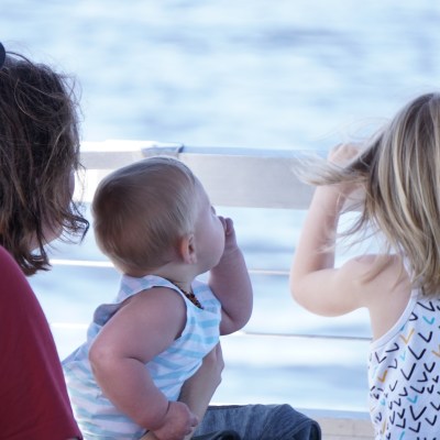 Family looking out at water; two adults, a baby, and a child leaning on a railing.