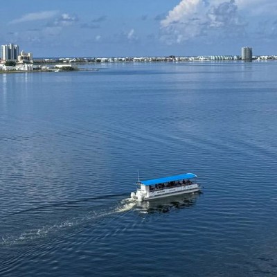 Boat with blue canopy on calm water with cityscape in background under cloudy sky.
