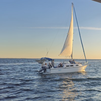 A sailboat with people onboard gliding on calm water during sunset.
