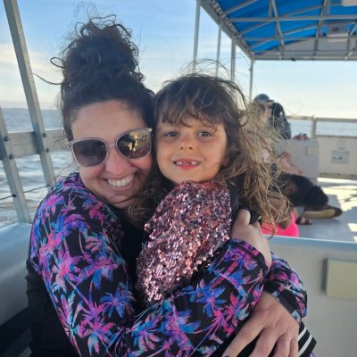 Woman and child smiling on a boat with a blue canopy on a sunny day.