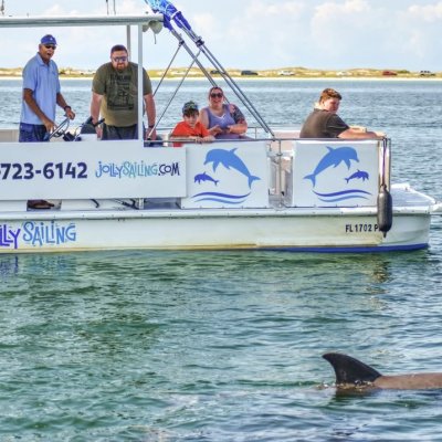 People on a boat watching a dolphin swim nearby.