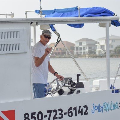 Smiling person steering a small boat with a blue canopy, near the shore.