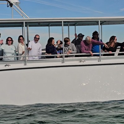 Group of people on a boat waving and pointing on a sunny day.