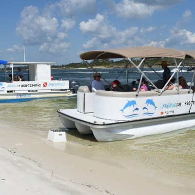 Two pontoon boats with passengers on a sandy beach under blue skies.