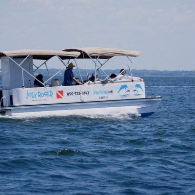 A covered boat with people cruising on a body of water under a clear sky.
