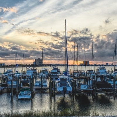 Boats docked at a marina during a cloudy sunset with buildings in the background.