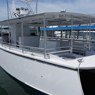 White fishing boat docked at a pier with a clear sky and distant buildings.