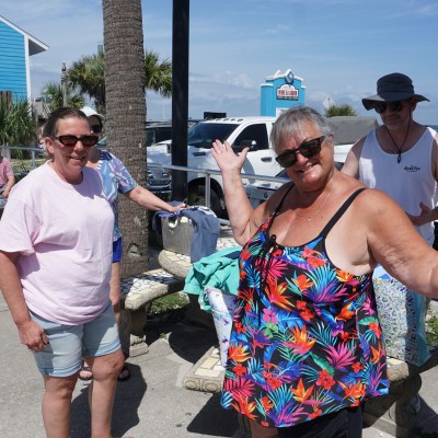 Two women smiling and posing outdoors near palm trees on a sunny day.
