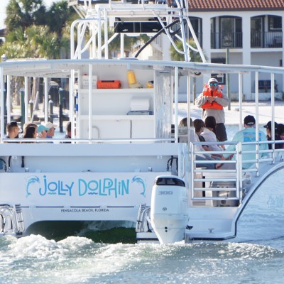 Back view of a tour boat named 'Jolly Dolphin' with passengers on a waterway.