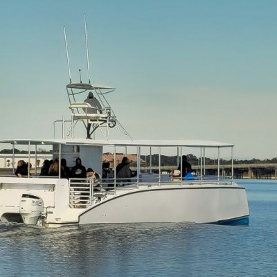 A white catamaran with passengers in calm waters near a bridge.