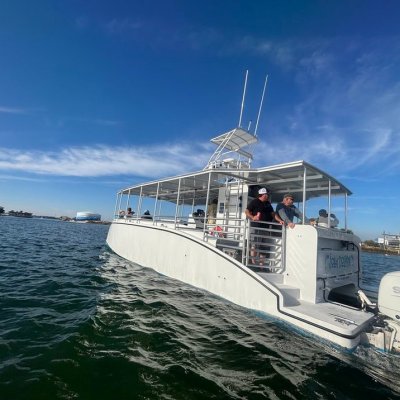 White boat with people aboard cruising on sunny water near shoreline buildings.