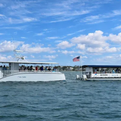 Two white boats with people on a blue sea under a cloudy sky, one flying an American flag.