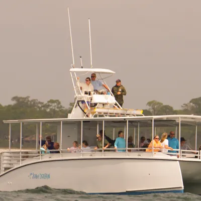 Catamaran with passengers on a calm sea near a wooded shoreline.