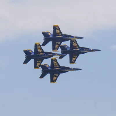 Four blue and yellow jets fly in close formation against a partly cloudy sky.