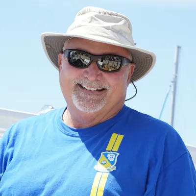 Man in blue shirt and hat smiling outdoors on a sunny day.