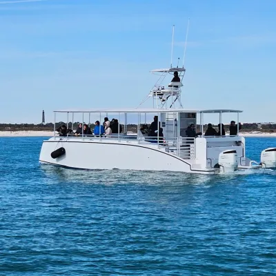 A white tour boat with passengers on calm blue water near a sandy shoreline.