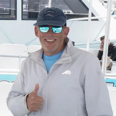 Man wearing sunglasses and a cap giving a thumbs up on a boat.