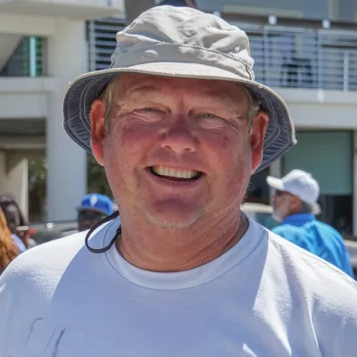 Smiling man in a bucket hat outdoors near a building.