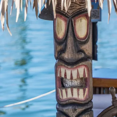 Carved tiki statue under a thatched roof by water.