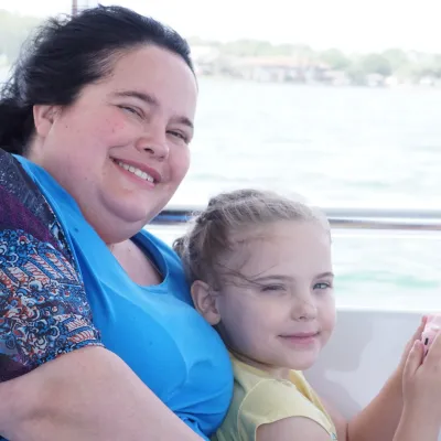 Smiling adult and child sitting on a boat with water in background.