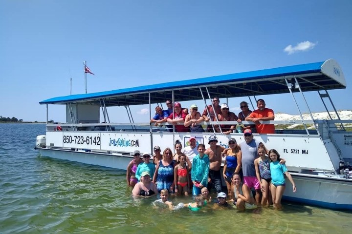 Group of people posing in water near a boat on a sunny day.