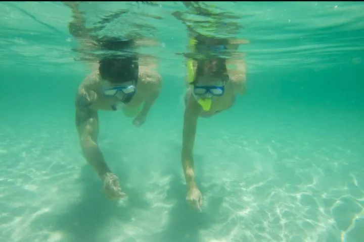 Two people snorkeling underwater in clear blue water.