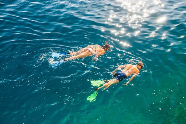 Two people snorkeling in clear blue water with sunlight reflecting on the surface.