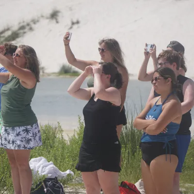 Group of people on a beach taking photos of something in the distance.
