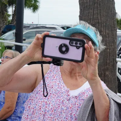 Woman taking a photo with smartphone in front of palm trees.