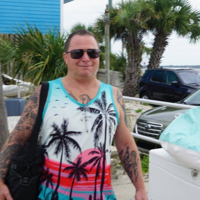 Person in colorful tank top walking near parked cars and palm trees.