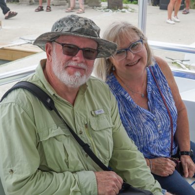 Two smiling people seated on a boat, outdoors.