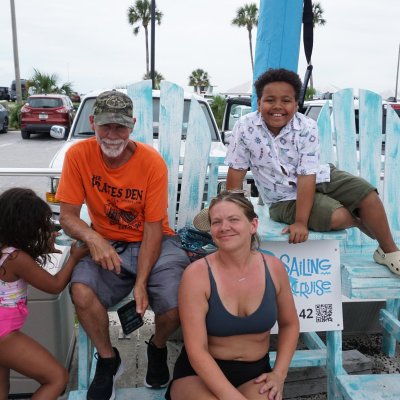 Group of four people smiling near large blue chairs by the beach.