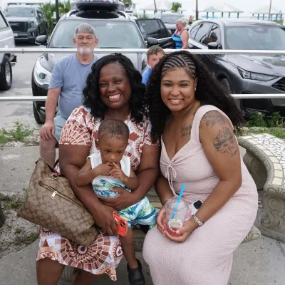 Two women and a child sitting outdoors, cars in the background.