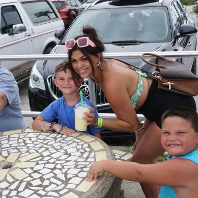 Group of people smiling at a mosaic table in a parking lot.