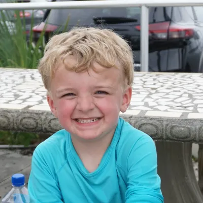 Smiling child in blue shirt sitting by mosaic table outdoors.