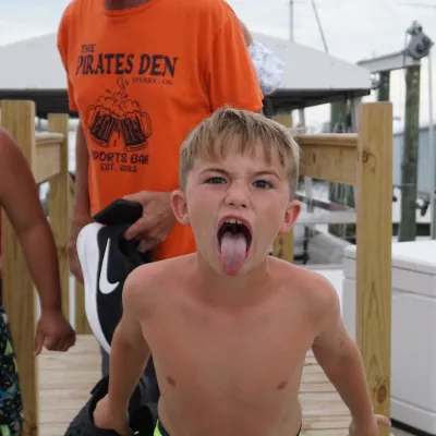 Two boys in swim trunks on a dock; one sticks out tongue playfully.