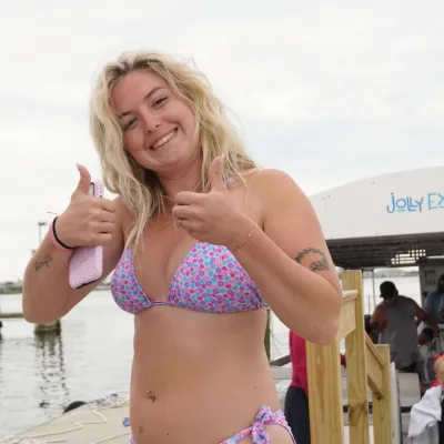 Person in a swimsuit giving thumbs up near a docked boat.
